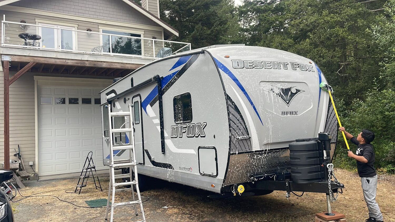 A Skagit Auto Detail crew member washing a Desert Fox travel trailer by hand with a long brush