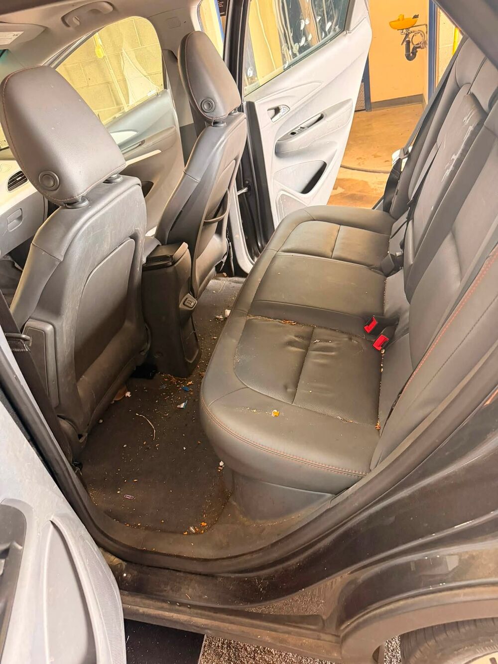Back seat and floor of a Chevrolet Bolt covered in crumbs, leaves and dirt before detailing